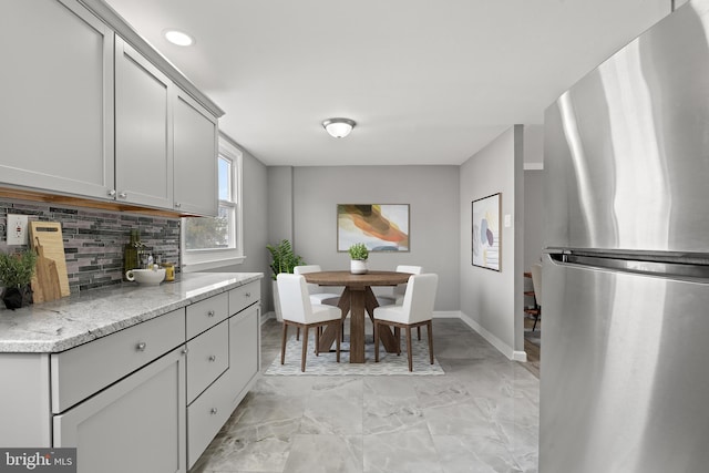 kitchen featuring baseboards, light stone countertops, decorative backsplash, freestanding refrigerator, and marble finish floor