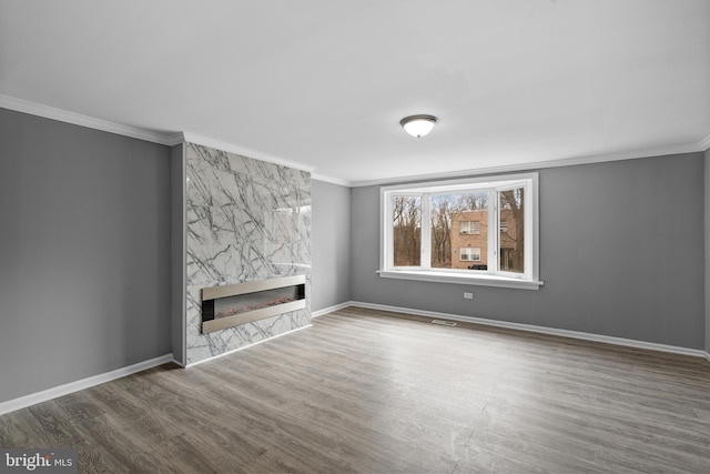 unfurnished living room featuring a premium fireplace, baseboards, wood finished floors, and crown molding