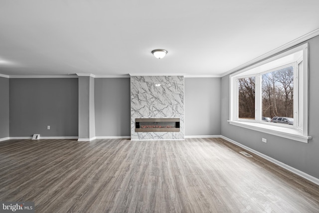 unfurnished living room with wood finished floors, visible vents, baseboards, a fireplace, and crown molding