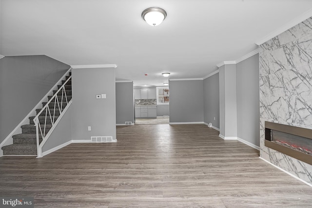 unfurnished living room featuring stairway, wood finished floors, visible vents, a fireplace, and crown molding