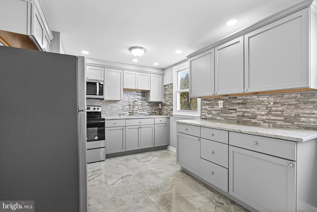 kitchen featuring backsplash, gray cabinets, appliances with stainless steel finishes, and a sink