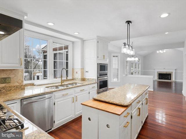 kitchen with dark wood finished floors, appliances with stainless steel finishes, a center island, white cabinetry, and a sink