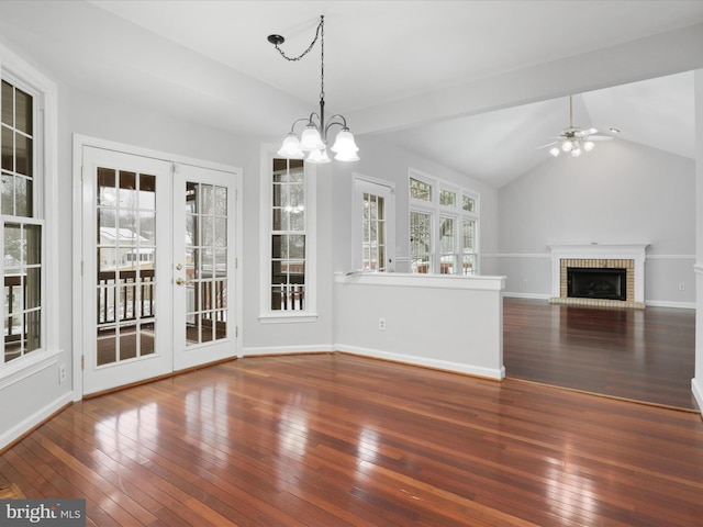 unfurnished dining area featuring lofted ceiling, dark wood-type flooring, french doors, a fireplace, and ceiling fan with notable chandelier