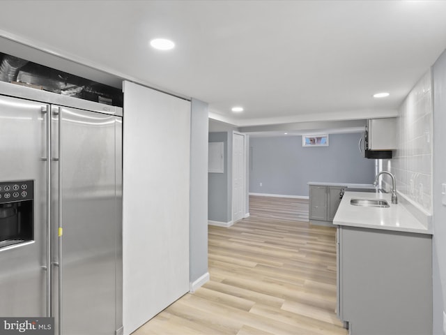 kitchen with a sink, baseboards, light countertops, stainless steel fridge with ice dispenser, and light wood finished floors