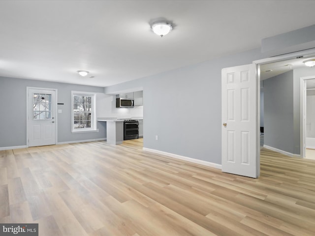 unfurnished living room with light wood-type flooring and baseboards