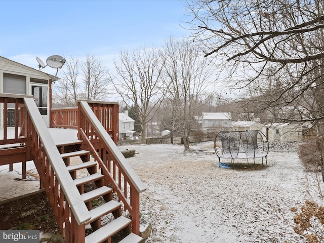 snowy yard featuring a trampoline, stairway, and a wooden deck