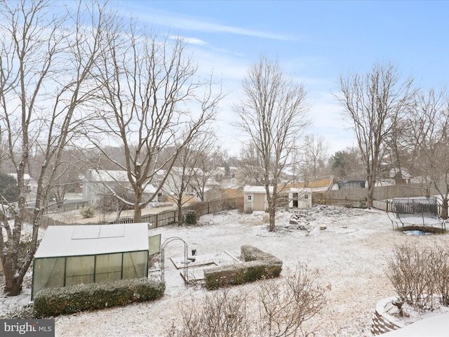 snowy yard with a trampoline, an outbuilding, and a fenced backyard