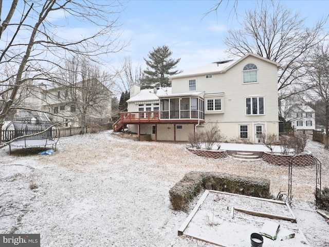 snow covered back of property with a sunroom, a chimney, a trampoline, fence, and a deck