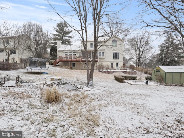 snowy yard featuring a wooden deck, a trampoline, an exterior structure, and an outbuilding