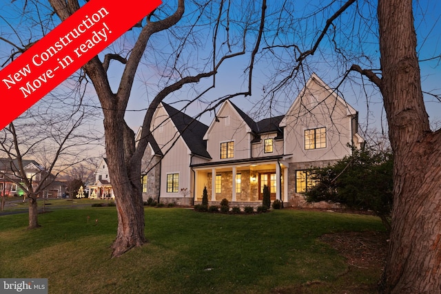 back of property at dusk featuring stone siding, a porch, and a yard