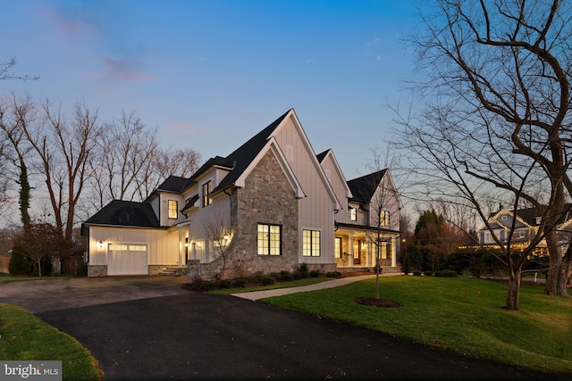 view of front of property with an attached garage, board and batten siding, a front yard, stone siding, and driveway