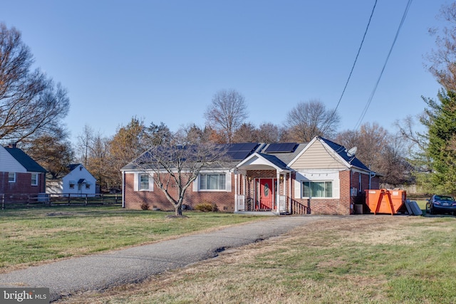 ranch-style house featuring fence, a front lawn, solar panels, and brick siding