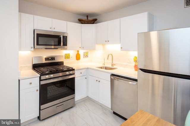 kitchen with marble finish floor, stainless steel appliances, light countertops, white cabinetry, and a sink