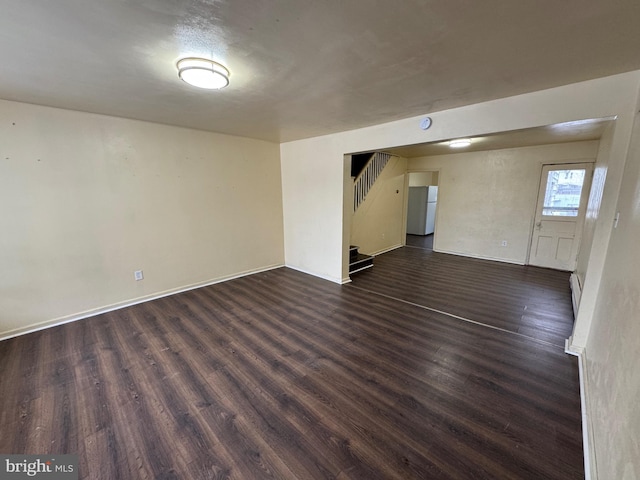 spare room featuring dark wood-style floors, stairway, baseboard heating, and baseboards