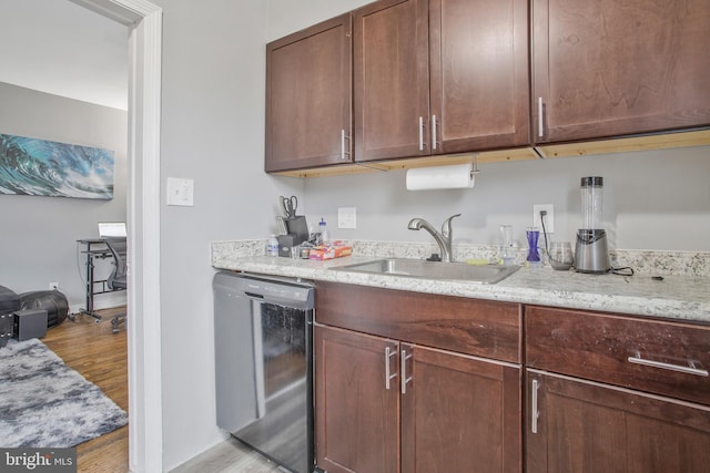 kitchen featuring black dishwasher, a sink, light stone countertops, and light wood-style floors