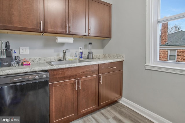 kitchen featuring baseboards, dishwasher, light stone counters, light wood-type flooring, and a sink