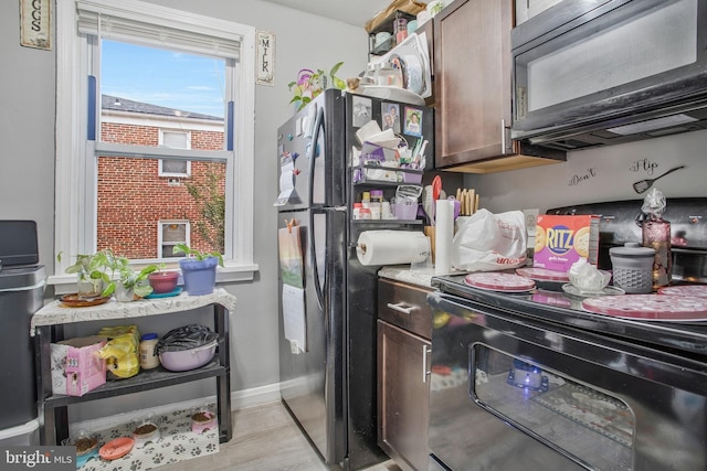 kitchen with light countertops, light wood-style floors, black appliances, dark brown cabinets, and baseboards