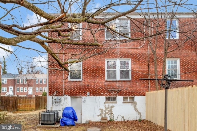 view of side of home featuring brick siding, fence, and central AC unit