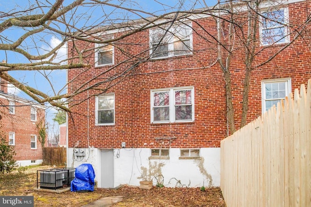 view of home's exterior with central AC, brick siding, and fence