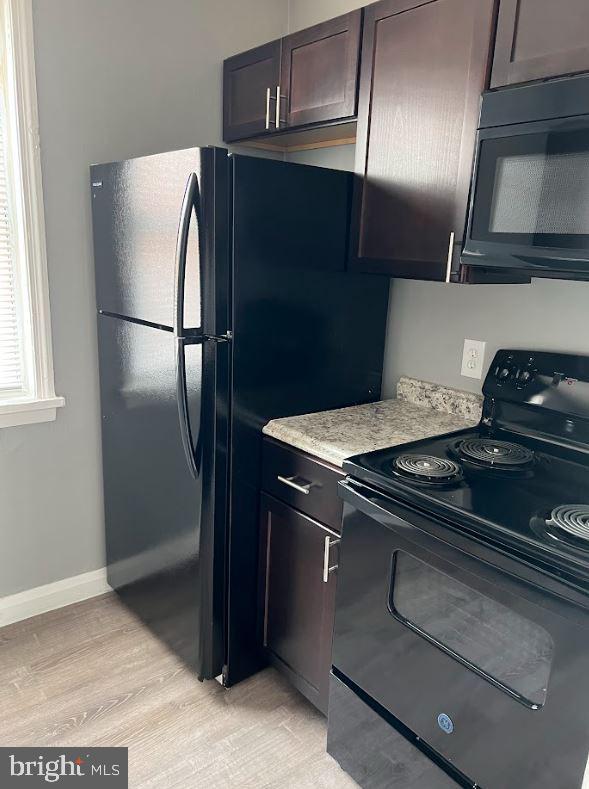 kitchen with light wood finished floors, light countertops, black appliances, dark brown cabinets, and baseboards