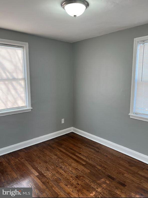 unfurnished room with dark wood-type flooring, a healthy amount of sunlight, and baseboards