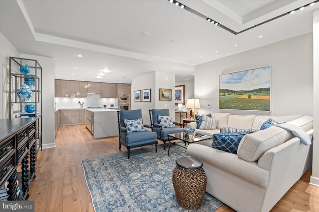 living room with light wood-style floors, recessed lighting, and a tray ceiling