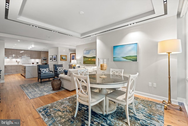 dining area with light wood-type flooring, a raised ceiling, and baseboards