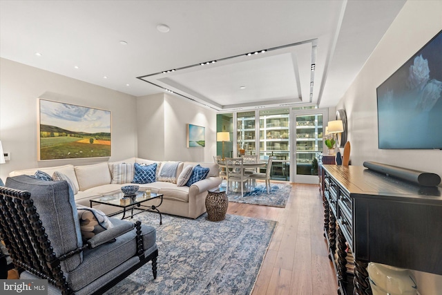 living area with wood-type flooring, a raised ceiling, and a wall of windows