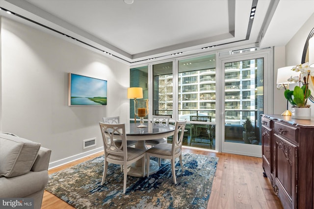 dining space featuring visible vents, a tray ceiling, hardwood / wood-style flooring, and baseboards