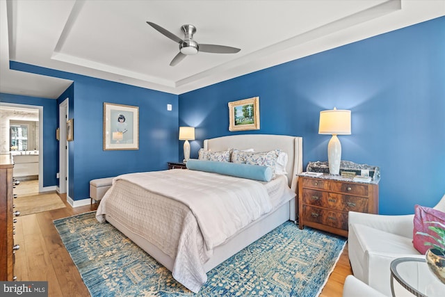 bedroom featuring a tray ceiling, a ceiling fan, hardwood / wood-style flooring, and baseboards