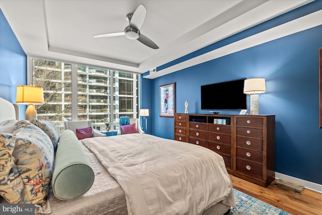 bedroom featuring wood finished floors, visible vents, a ceiling fan, baseboards, and a wall of windows