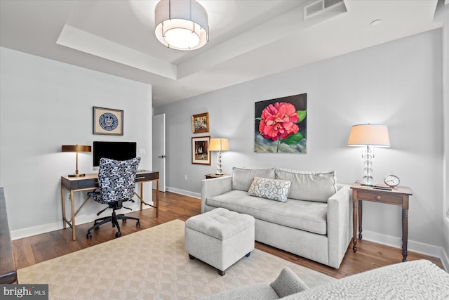 living area with a tray ceiling, visible vents, baseboards, and wood finished floors