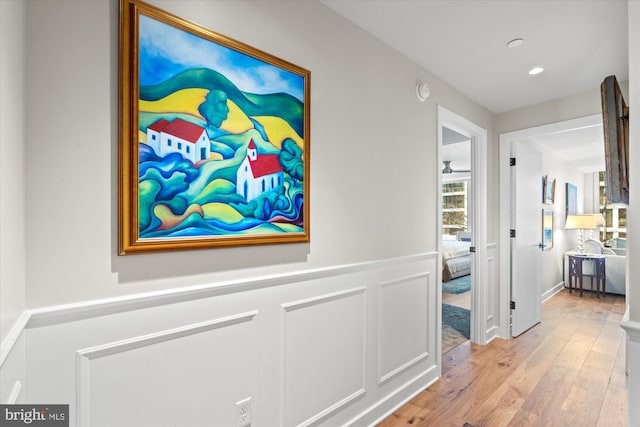 hallway featuring recessed lighting, wainscoting, a decorative wall, and light wood-style flooring