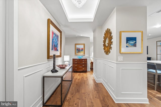 hall featuring a wainscoted wall, a decorative wall, and wood finished floors