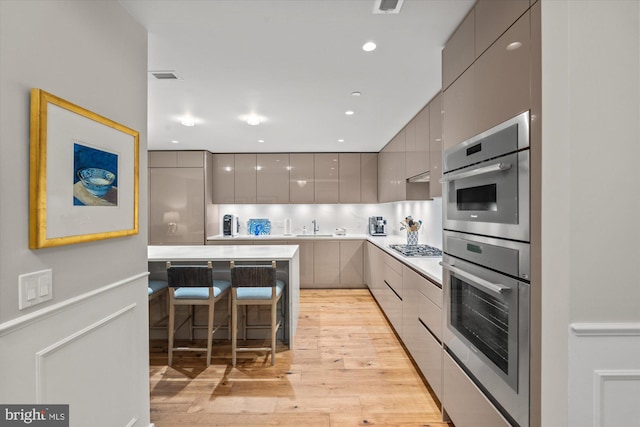 kitchen featuring stainless steel appliances, gray cabinets, light wood-style floors, modern cabinets, and a kitchen bar