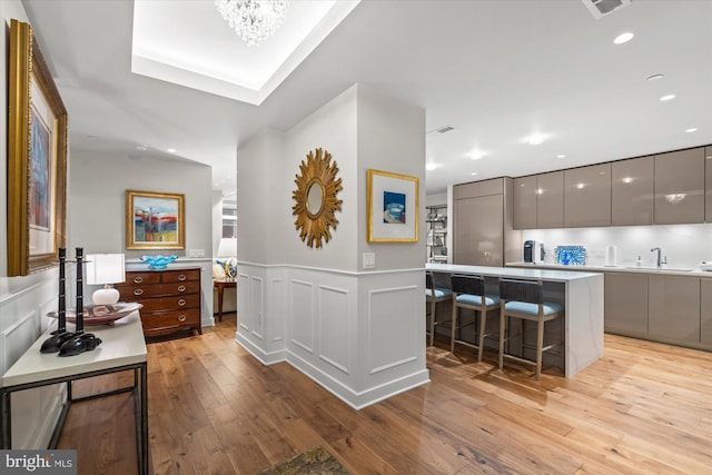 hall featuring recessed lighting, a wainscoted wall, a decorative wall, a sink, and light wood finished floors