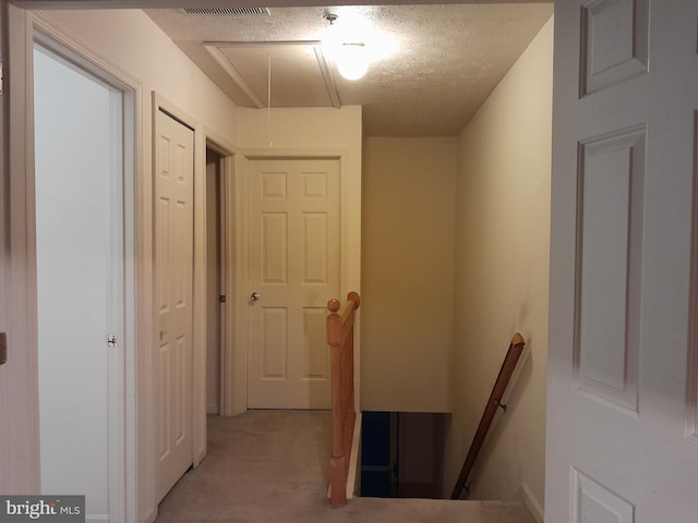 corridor with attic access, light colored carpet, a textured ceiling, and an upstairs landing