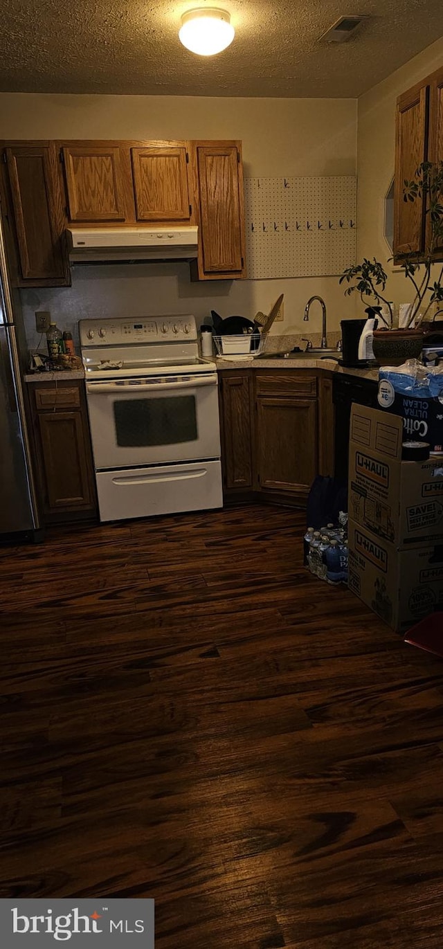 kitchen with a textured ceiling, under cabinet range hood, freestanding refrigerator, dark wood-style floors, and white range with electric cooktop