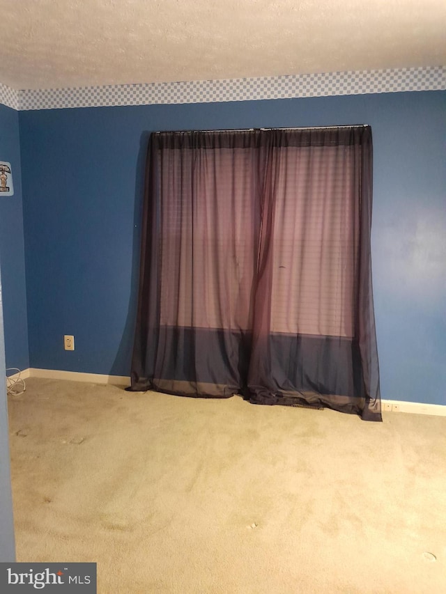 carpeted spare room featuring a textured ceiling and baseboards