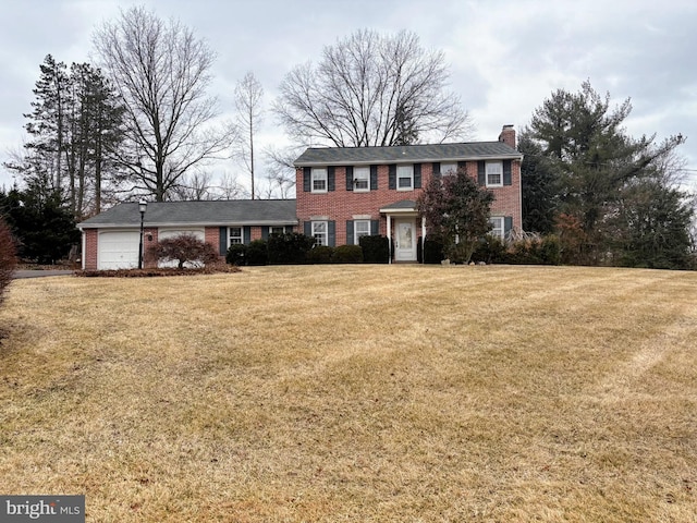 colonial-style house with a garage, brick siding, a chimney, and a front yard