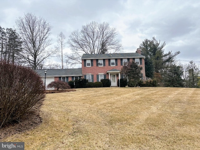 colonial house with a front lawn, a chimney, an attached garage, and brick siding