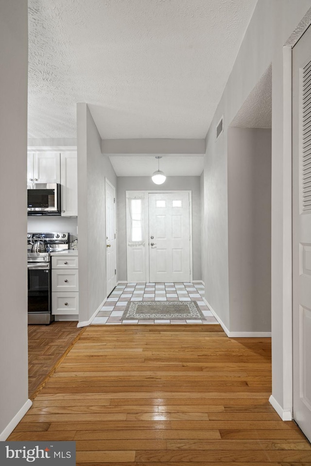 foyer entrance with baseboards, visible vents, light wood finished floors, and a textured ceiling