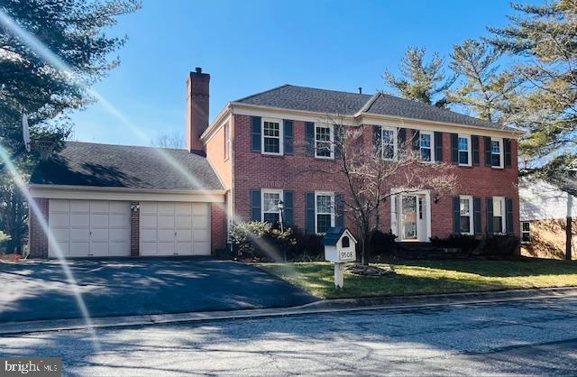 colonial-style house featuring an attached garage, a chimney, a front lawn, aphalt driveway, and brick siding