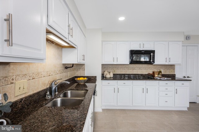 kitchen with a sink, dark stone counters, black appliances, and white cabinets