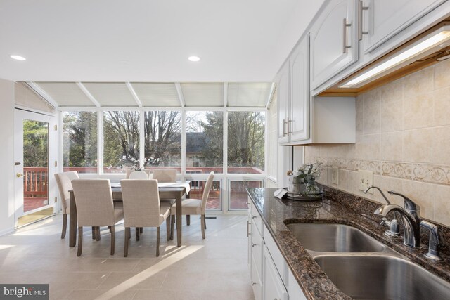 kitchen featuring decorative backsplash, dark stone countertops, white cabinetry, and a sink