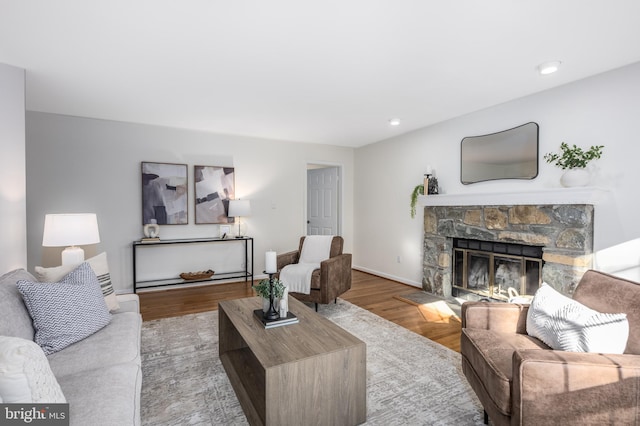 living room featuring a stone fireplace, recessed lighting, and wood finished floors