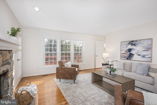 living area with a stone fireplace, visible vents, baseboards, and light wood finished floors