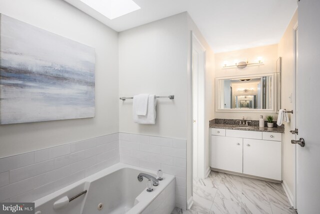 bathroom with vanity, a jetted tub, a skylight, and marble finish floor