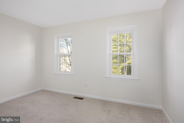 carpeted empty room featuring a wealth of natural light, visible vents, and baseboards