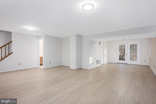 unfurnished living room featuring visible vents, baseboards, stairs, and light wood-style floors